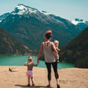 mother and children walk near lake surrounded by mountains