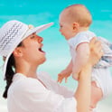 woman wearing white hat holding up and laughing with her baby on the beach