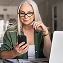white-haired woman with phone and computer