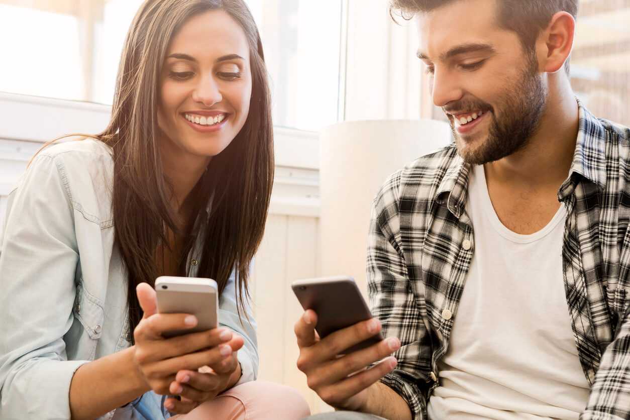 man and woman looking at their phones and smiling