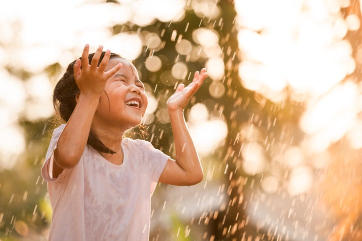 Happy little girl with autism having fun playing in a sprinkler