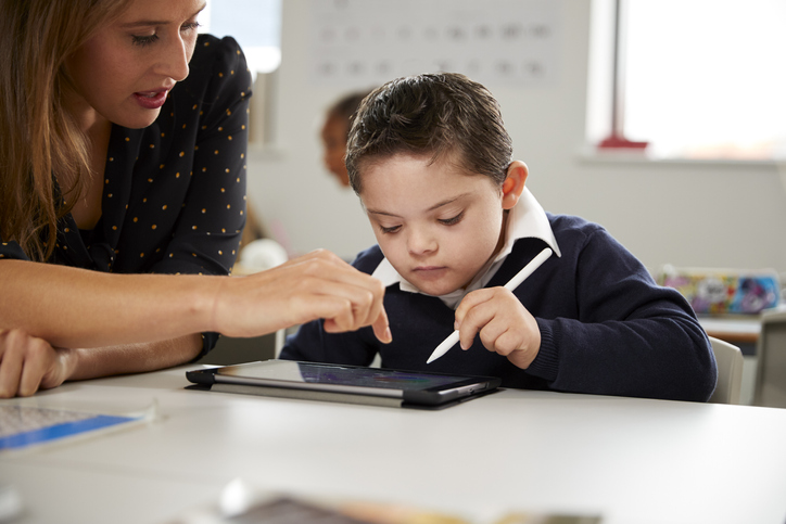 boy with disabilities working on a tablet receiving extra help from teacher