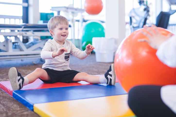 physical therapist works with a young boy with autism in an open floor clinic