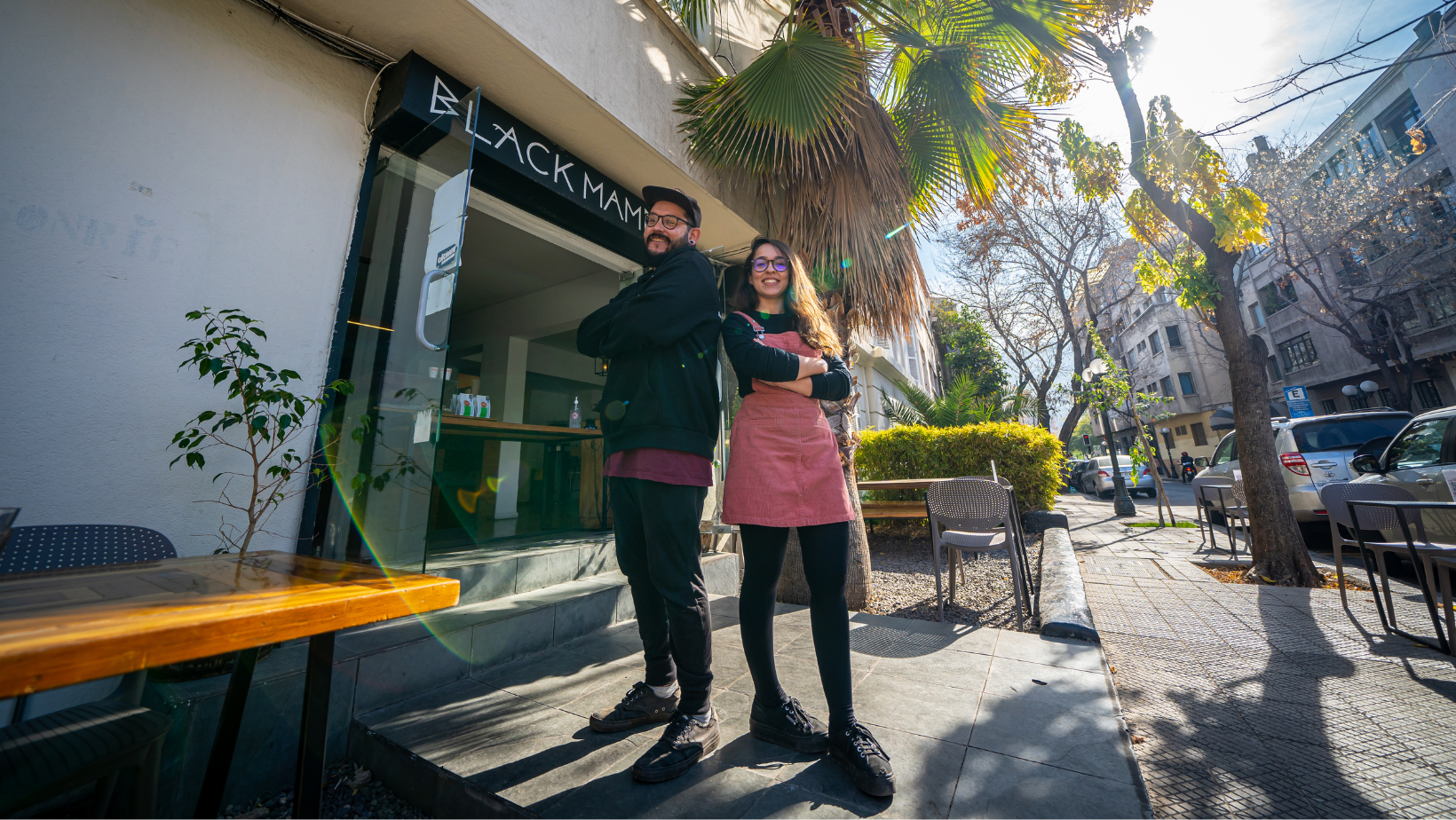 Paloma y Nicolás posando frente a la puerta de entrada de cafetería Black Mamba. 