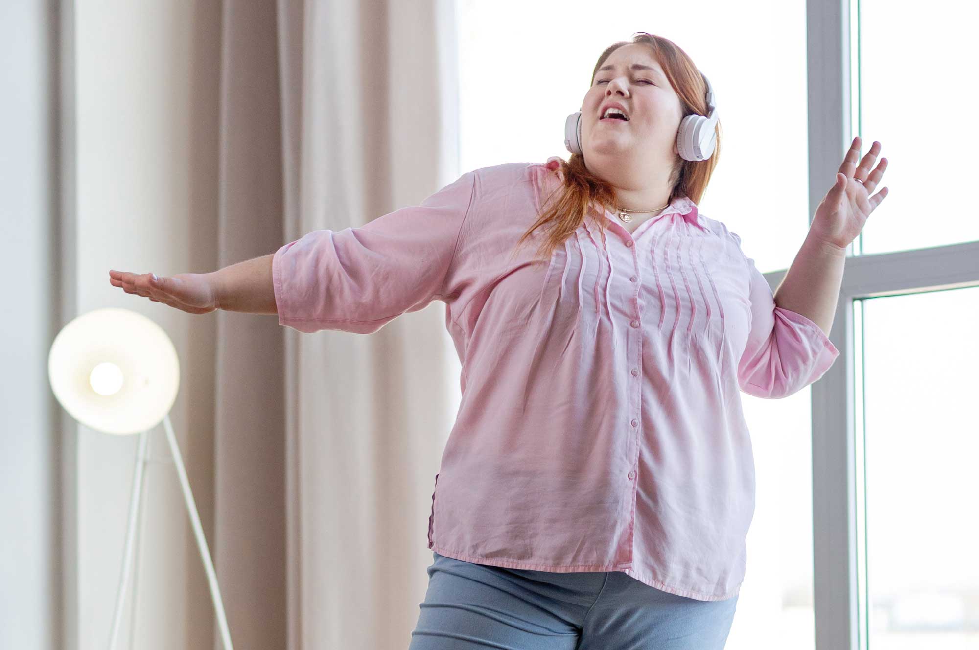 Frau mit Kopfhörern tanzt fröhlich vor einem Fenster.