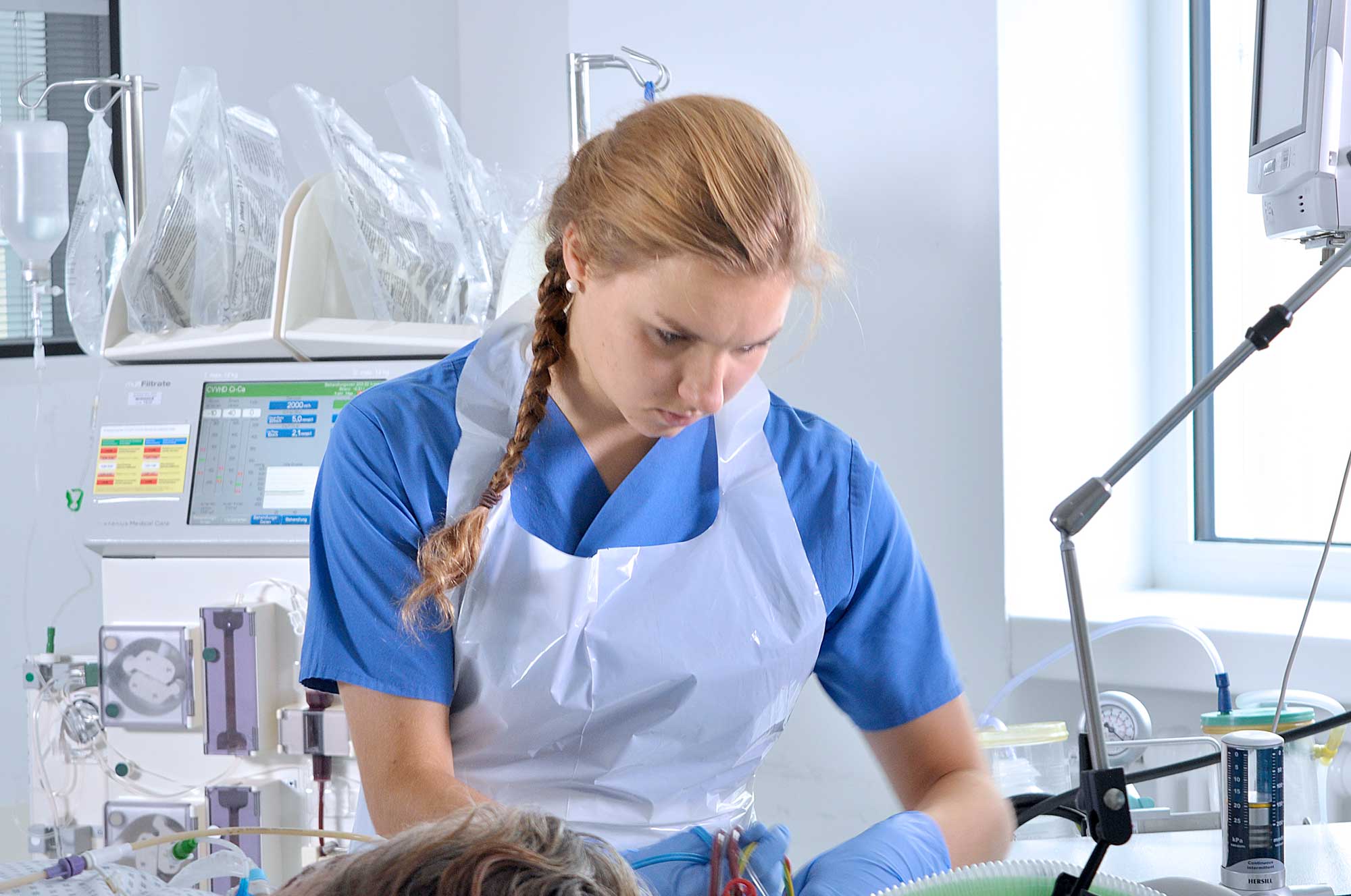 Pflegekraft in blauer Kleidung arbeitet konzentriert an medizinischen Geräten