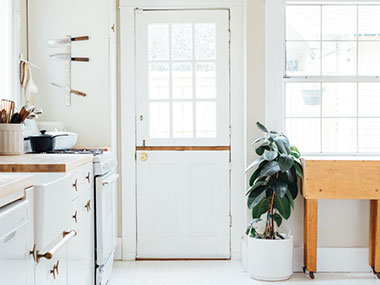 Interior of a fixer-upper kitchen with dated white cabinets and a plant by the door