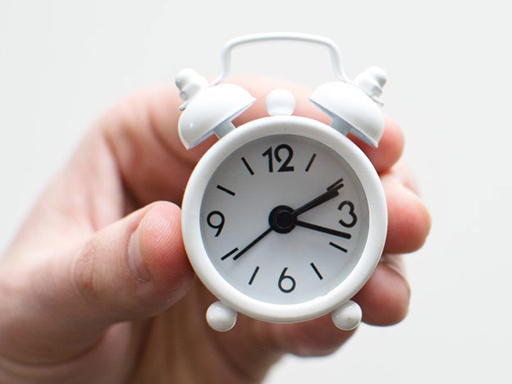 A hand holding a tiny alarm clock