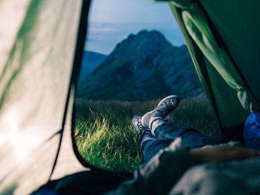 Person laying their tent with feet outside facing a mountain