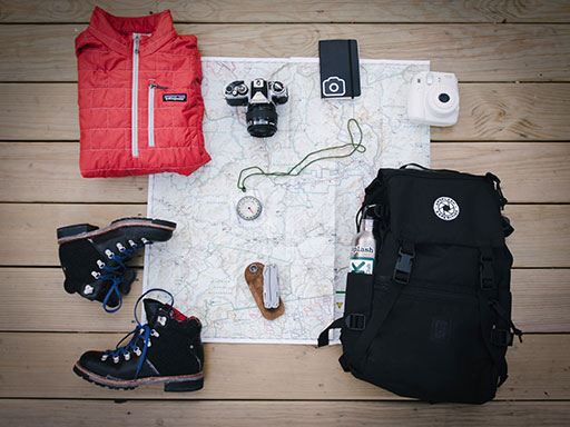 A red vest, hiking boots, backpack, and other camping items displayed over a map