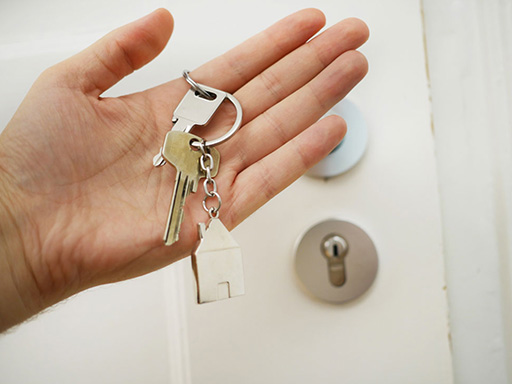 Hand holding a house key in front of a padlocked door