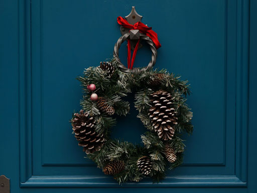 A pinecone and pine wreath hanging on a blue door